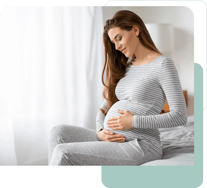 Pregnant woman sitting on bed, smiling gently.